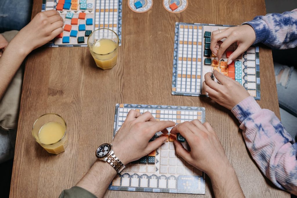 people-playing-an-azul-board-game-8111357 Close-up of hands and board game tiles during a fun gaming session indoors.